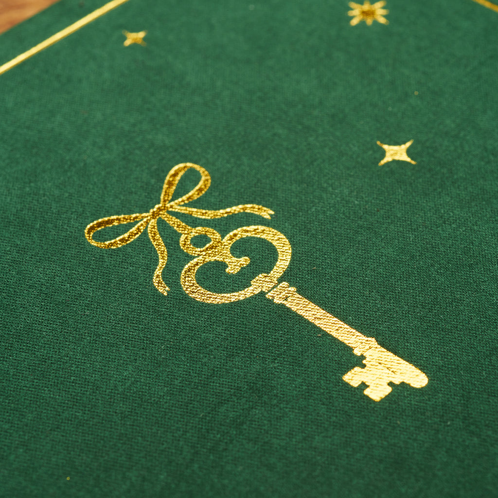 Gold-foil key design pressed into soft green velvet cover, showing fine border detail.