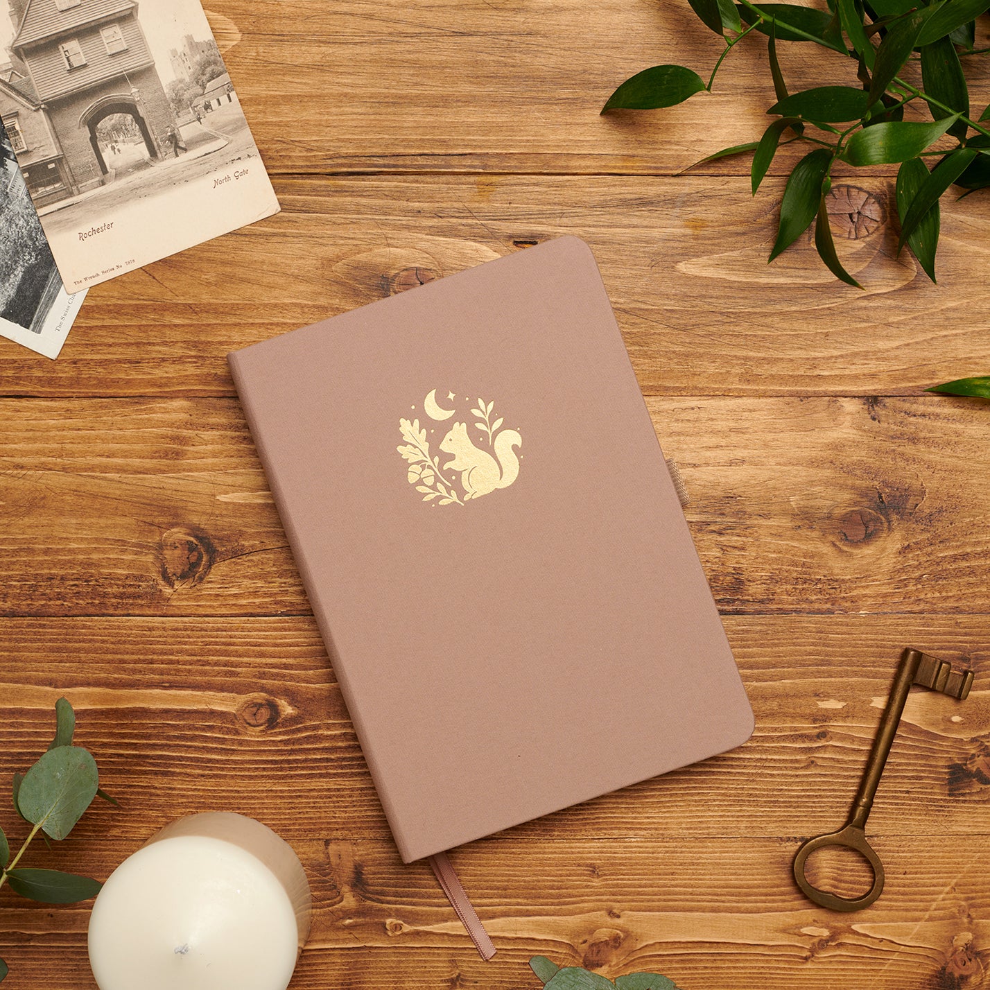 Forage Treasures dotted notebook—fawn linen cover with gold-foil squirrel on wooden desk, compass and photos.