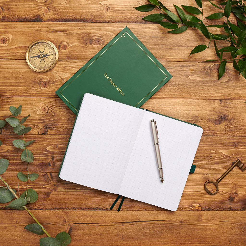 Open dotted journal beside its matching box on wooden desk showing lay-flat binding and soft dot-grid pages.