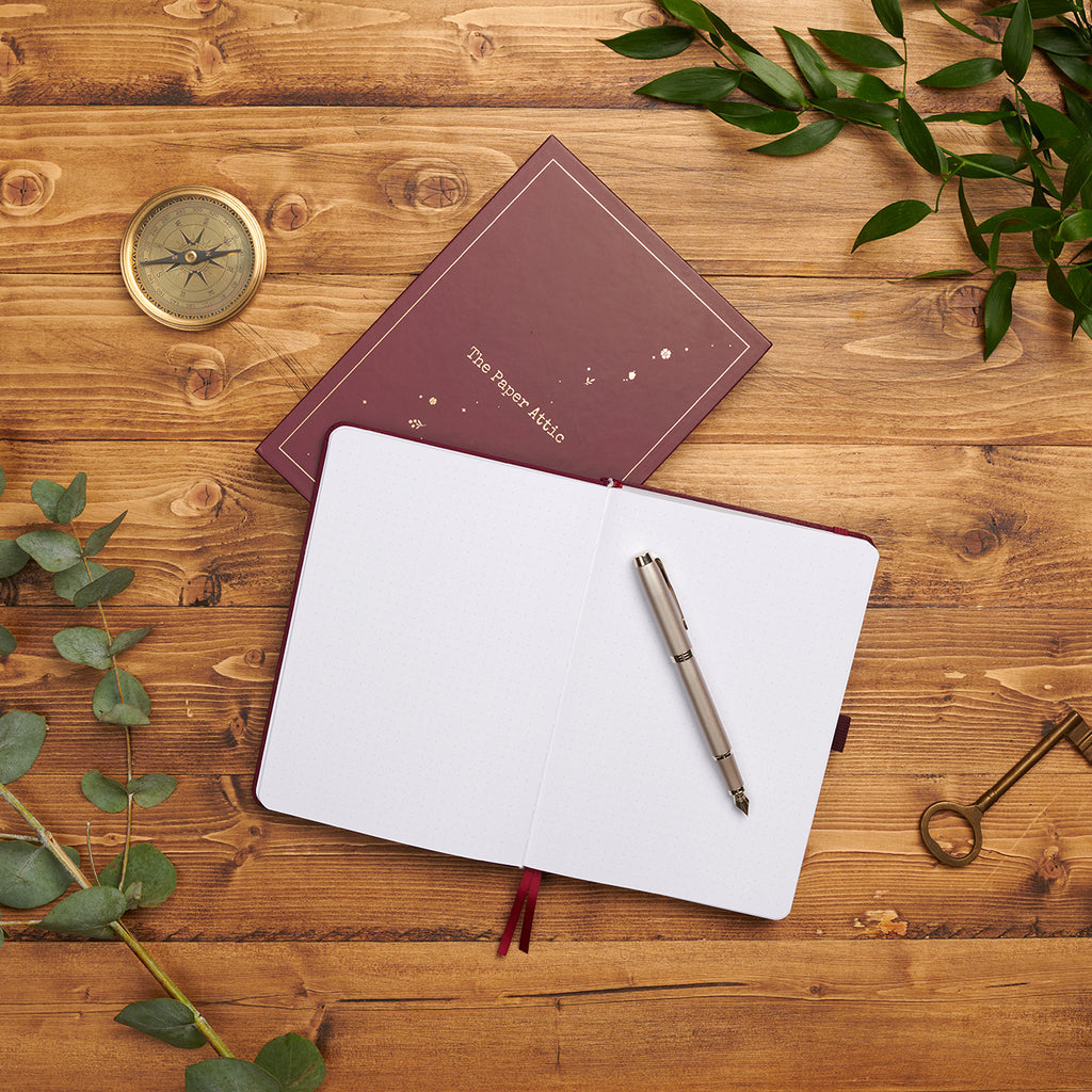 Open dotted journal beside its matching box on wooden desk showing lay-flat binding and soft dot-grid pages.